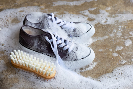小白鞋装有粉末洗涤水溶解泡沫的运动鞋和水泥地板上的木刷子洗脏鞋背景
