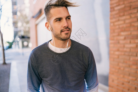 英俊的年轻男子在街上用耳机听音乐的肖像城市概念图片
