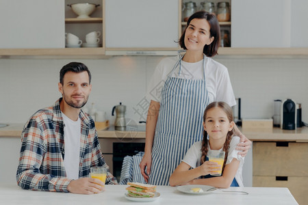 由母亲父和女儿组成的家庭在现代厨房里一起摆装喝新鲜果汁吃哀痛药享受家庭气氛图片