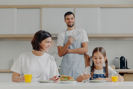 父亲站在后面为家庭准备美味的菜盘友善家庭成员周末在厨房聚会享受愉快的谈话图片