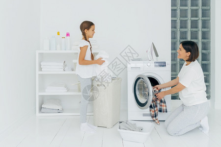 快乐的母亲和女儿在家里忙着洗衣服快乐的面孔黑发女人的洗衣机图片