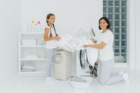 母亲和女儿在洗衣房服在房里用板上装服妇女跪在洗衣机旁边图片