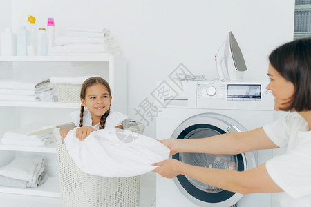 与母亲一起在洗衣房玩乐帮助洗衣服妇女装上洗衣机在家过周末忙务活图片
