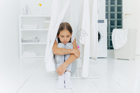 沉思的寂寞悲伤小女孩坐在洗衣房的地板上图片