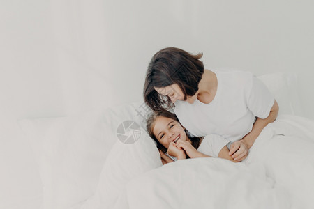 快乐的母亲和女儿一起在床上玩得开心有快乐的表达方式享受软睡衣的舒适有快乐外表在卧室里过夜图片