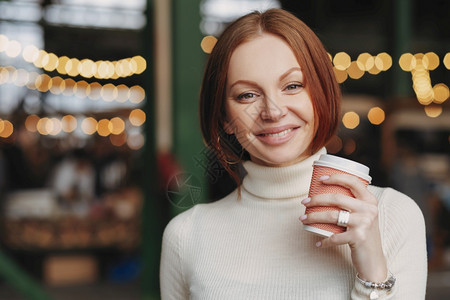 有吸引力的年轻女照片持有外卖咖啡喜悦的表情牙齿笑容穿着白色的跳跃衣图片