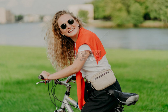 身穿休闲服的女子骑着自行车在河道边图片