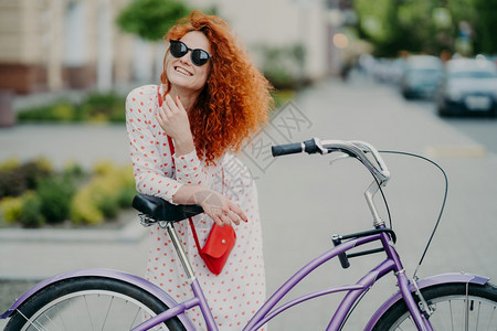 快乐的卷妇女关注距离在城市骑自行车享受爱好戴遮光和长裙有红小袋图片