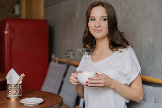 怀着梦幻般的表情美丽黑发女下班后有咖啡休息穿白色T恤衫在咖啡店闲暇时间享受娱乐图片