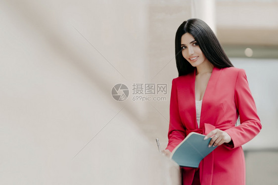 身着优雅红色服装的美丽微笑女士在笔记本上写下一些笔记站在外面复制左边的空间用于宣传内容商业女人与合伙或同事会面图片