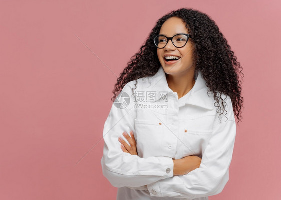 美女穿着白色夹克保持手臂折叠看一笑得迷人与朋友一起享受愉快的天站在粉红色的墙边空间图片