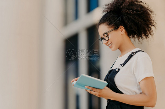 专注组织者拍摄的卷发女孩剖面图了解她下周的计划有正面表情戴光眼镜白T衬衫和穿衣服图片