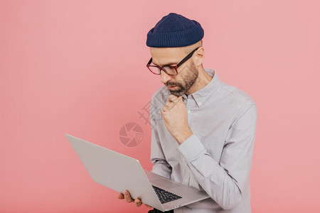 有经验的男自由职业者制定了新的战略拥有现代笔记本电脑保持下巴的手势穿正规服装忙于远距离工作与粉红色背景隔绝复制空间图片