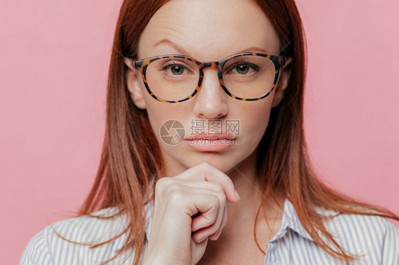 女企业主自信的贴近肖像拿着下巴抬眉戴光眼镜黑发穿着优雅衬衫认真看摄影机棚模特图片