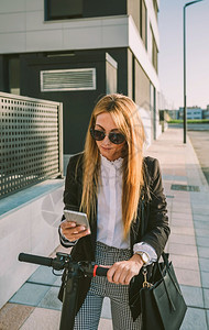 拥有电子摩托车的女商人在街上看手机图片