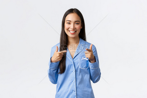 带着充满自信的欢乐表情白色背景可爱的亚洲女孩笑着快乐站在蓝色睡衣中邀请女友们在果酱中过夜派对图片
