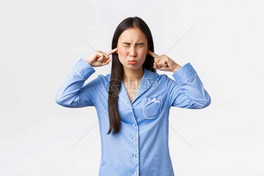 穿着蓝睡衣的傻亚洲女孩憎恨骚扰声音闭上耳朵和眼睛憎恶不满意抱怨吵闹的噪音图片