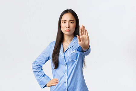 穿着蓝睡衣的严肃亚洲女孩伸出手来表明停止禁行动发出警告和反对不良行为禁止与白色背景相比的东西穿着蓝色睡衣的严肃亚洲女孩伸出手来表图片