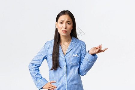 穿着蓝睡衣的持怀疑和沮丧亚洲女孩抱怨争论某事皱眉和举起手无法理解发生了什么图片
