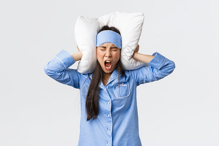 愤怒的亚洲女孩穿着睡衣和面具躺在床上用枕头闭耳朵大声叫喊因为吵得睡不着邻居在晚上通过聚会抱怨烦人的声音愤怒亚洲女孩穿着睡衣和面具图片