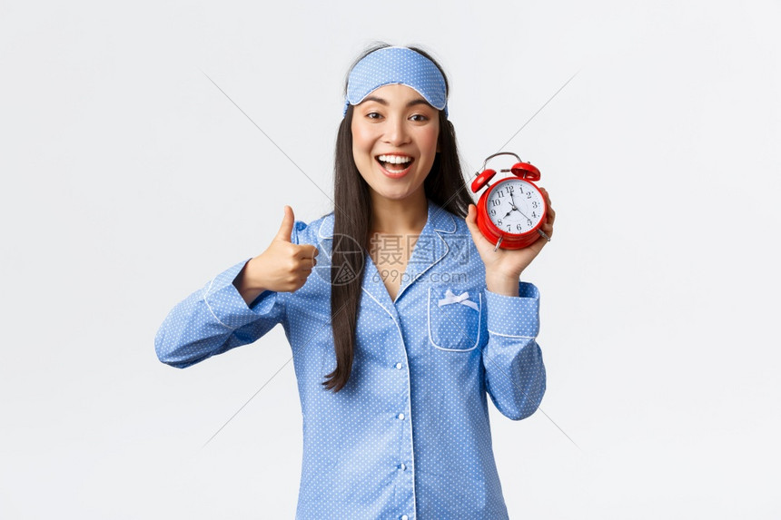 穿着蓝睡衣和面具的充满热情和快乐笑的亚洲女孩展示警钟和拇指表示他们赞同像是早起床积极和健康的生活方式充满热情和快乐的笑亚洲女孩穿图片