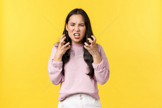 愤怒和的亚洲女孩 看着疯狂和侵略性的紧身拳头 想要凶恶的愤怒站立黄色背景 生活方式、情绪和广告概念图片