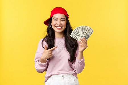 满意的年轻女孩知道如何在网上挣钱黄色背景人们的情感生活方式闲暇和美丽概念快乐的20岁女在红帽子上挣钱自豪地点着现金图片