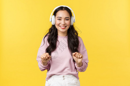 充满热情的有吸引力韩国女孩用无线耳机跳舞和微笑广泛聆听最喜爱的歌曲黄色背景人们的情感生活方式休闲和美丽概念充满热情的有吸引力韩国图片