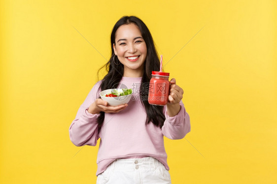 友好和快乐的亚洲女孩伸出手给你拿着沙拉分享午餐一起吃黄色背景人们的情感健康生活方式和食物概念友好和快乐的亚洲女孩伸出手给你黄色背图片