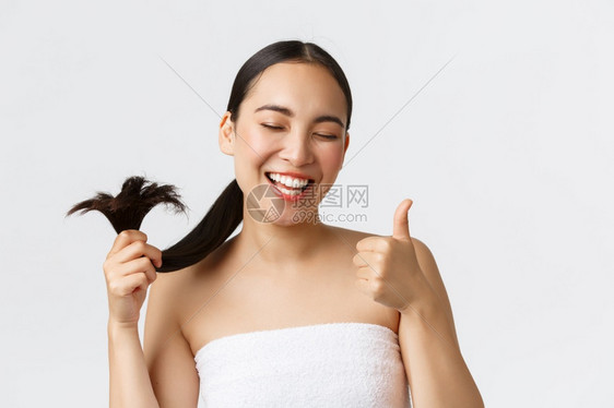 美貌脱发产品洗水和理护概念令人满足高兴的亚洲女孩在浴巾上露出拇指和健康的头发站立愉快的白色背景美丽洗发水和理护概念满意高兴的亚洲图片