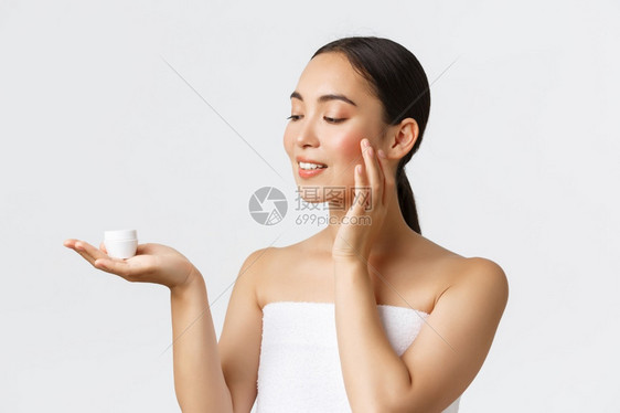 美貌个人护理温泉沙龙和皮肤护理概念美貌的年轻女站在浴巾上将奶油放在棕榈上将奶油涂在皮肤上摩擦脸美貌温泉沙龙和皮肤护理概念美貌的年图片