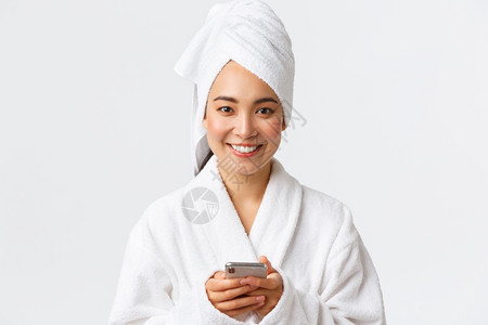 身穿浴巾和袍用手机微笑的相站立身穿浴巾和袍用微笑的相机站立身穿个人护理妇女美容洗澡和淋浴的概念身穿浴巾和袍用手机站立微笑的相机图片