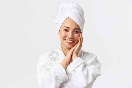 穿着毛巾和浴袍的美丽亚洲人女子轻地抚摸面部微笑着的白牙皮肤护理和卫生用品的推广个人护理妇女美貌洗澡和淋浴概念穿着毛巾和浴袍的美丽图片
