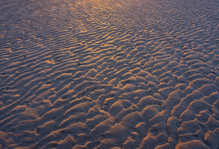 在日落的温暖光照下沙滩上波的抽象模式图片