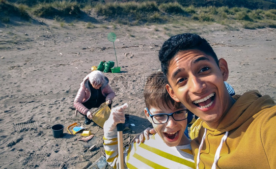 年轻人和男孩用移动式自拍而一群志愿者打扫海滩年轻人和男孩用自拍一群志愿者打扫海滩图片