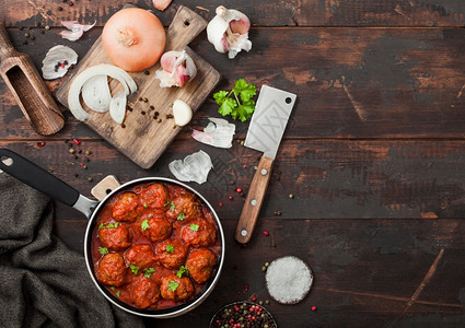 番茄酱里的传统肉丸煎锅里有辣椒大蒜和面食木板上有洋葱和切刀图片