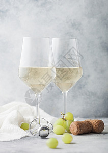 两杯白自制葡萄酒上面有软木和葡萄放在光桌底图片
