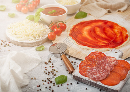 准备用生面粉烤番茄比萨饼沙拉米辣焦索切轮机新鲜西红柿和浅桌上的烤肉碗盘配奶酪和番茄糊图片