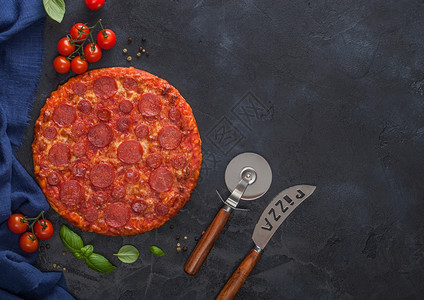 鲜烤热辣披萨配有切轮刀和子配有西红柿和黑餐桌底的烤肉图片