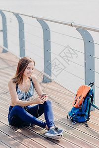 有吸引力活跃的年轻女垂直拍摄的有吸引力活跃年轻女拥有现代手机冲浪社交网络听耳机音乐周末享受闲暇时间听好友的留言图片