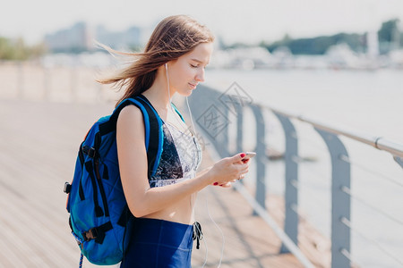 认真看着智能手机屏幕收听电子书携带背包在户外摆布长步行路呼吸新鲜空气享有平静氛图片