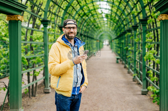 留胡子的男学生长有时装穿着站在绿色背景下使用手机载视频图片