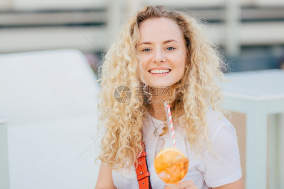 可爱的年轻女有牙色微笑新鲜的皮肤蓝眼睛喝夏新鸡尾酒快乐地看着相机在暑假期间和朋友一起休息令人难忘图片