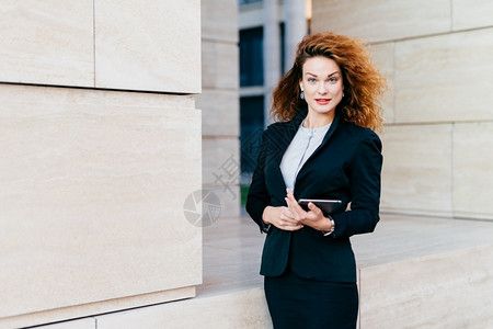 穿着优雅衣服头发丰满在上班时手握平板电脑的年轻成功女商人图片