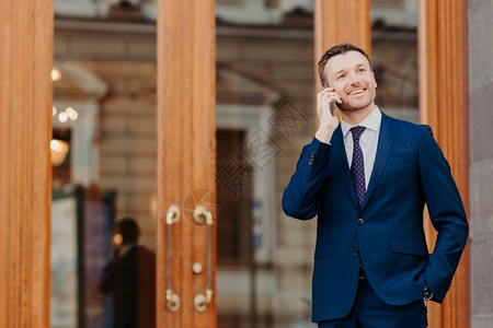 男与银行经营者协商通过手机进行交易身着正式西装手持口袋微笑积极站在餐馆门或入口附近图片