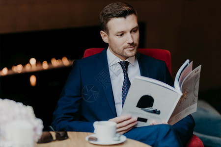 男创业者阅读商杂志坐在咖啡店喝或茶穿正式西装在就职后有晚餐休息和背景图片