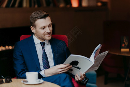 快乐的男昏迷主人肖像读杂志睡在舒适的咖啡店有快乐的表情下班后休息穿着正式衣服图片