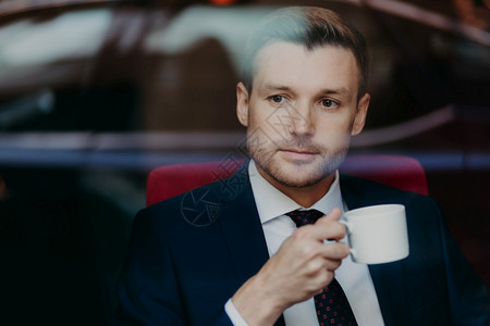 成功繁荣的男创业者照片上面有碎块思考一些东西穿正式衣服喝咖啡放在窗户上等待餐厅的生意伙伴图片