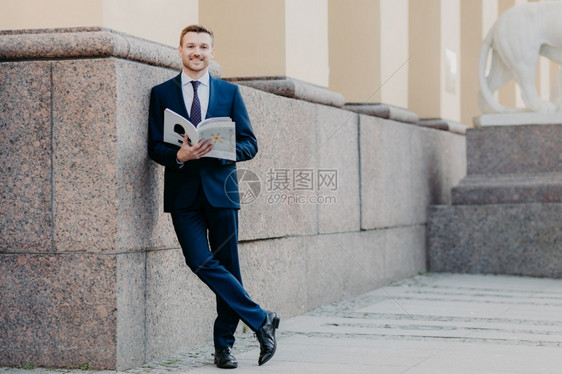 成功男老板照片的男老板横跨双腿持有商业杂志阅读必要的信息准备在同事面前展示站在办公大楼附近正式着装图片