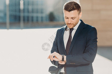 帅的男检查时间为商业会议赶时间看着手表穿正式的黑色西装在办公室大楼附近户外出现人商业和职概念图片